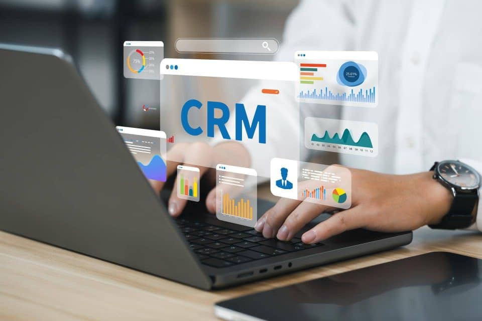 Person using a laptop with CRM and analytics graphics displayed on the screen.